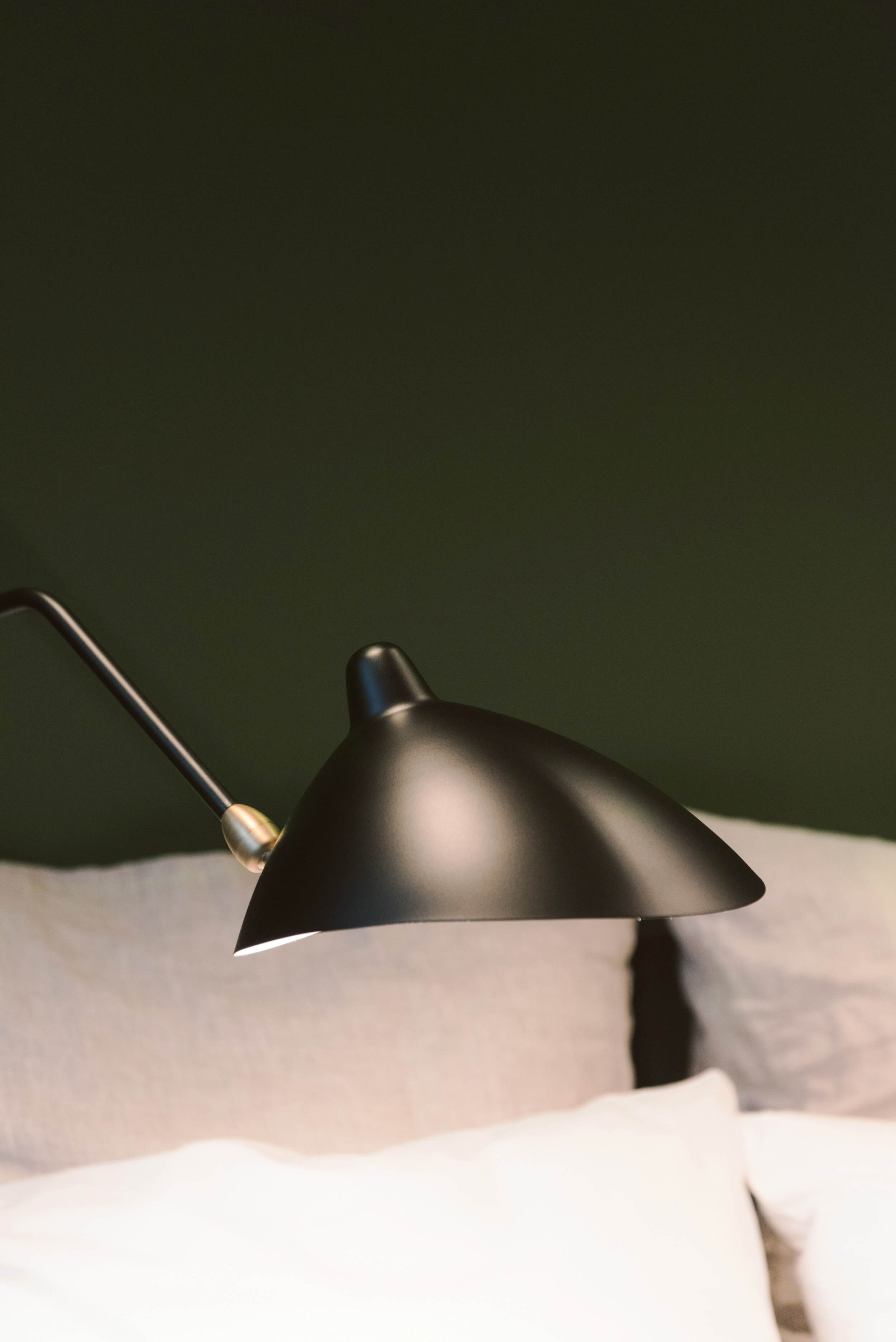 A contemporary black wall lamp above a brightly covered bed