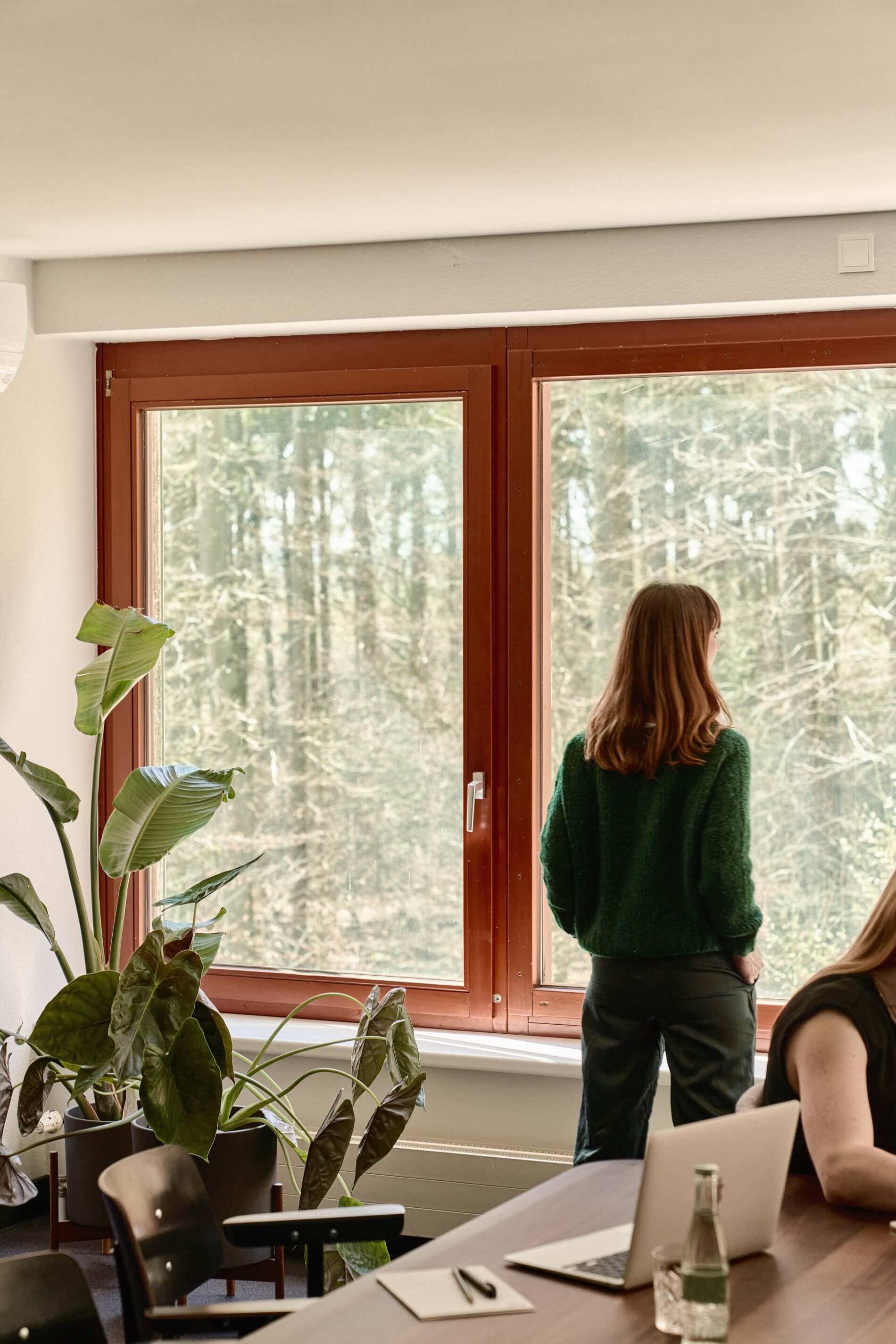 Eine Frau steht an einem Fenster in einem der Tagungsräume des Bold Campus und blickt in den Wald hinaus
