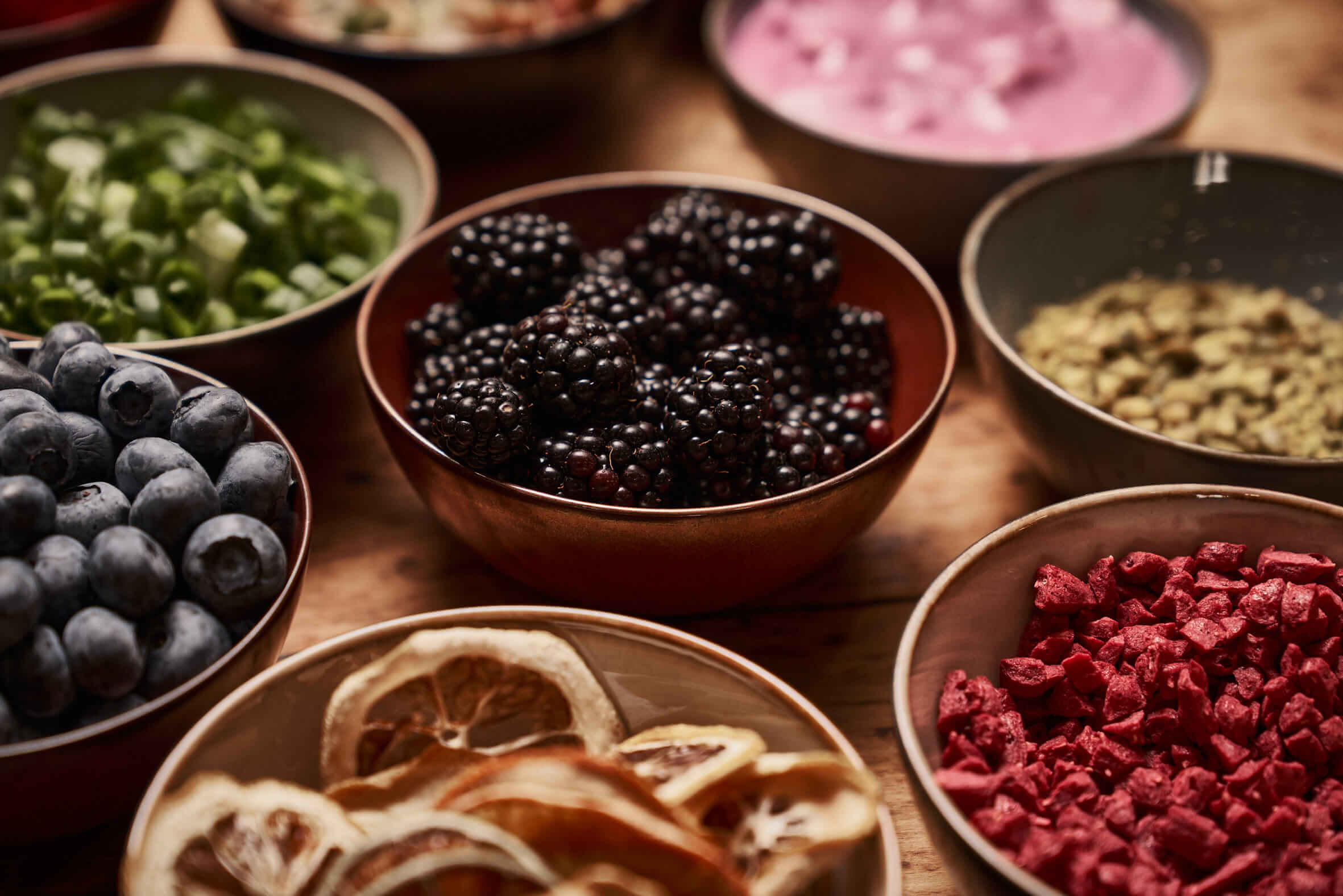 A collection of bowls with different contents such as blackberries, blueberries, yoghurt, pumpkin seeds and more. 
