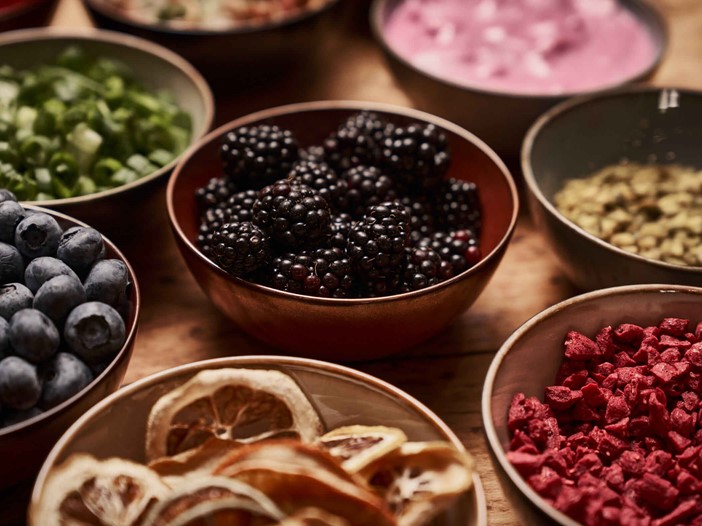 A collection of bowls with different contents such as blackberries, blueberries, yoghurt, pumpkin seeds and more. 