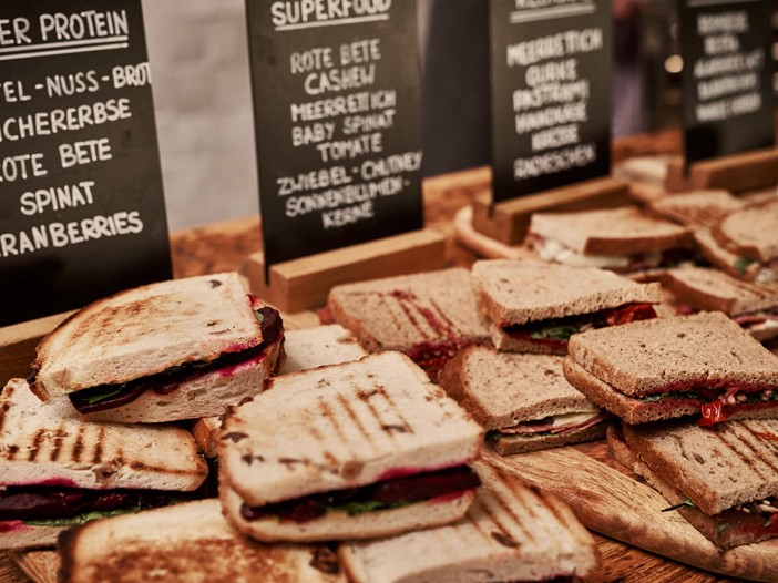 Sandwiches with various colourful toppings in a display, behind them boards with handwritten details of the ingredients