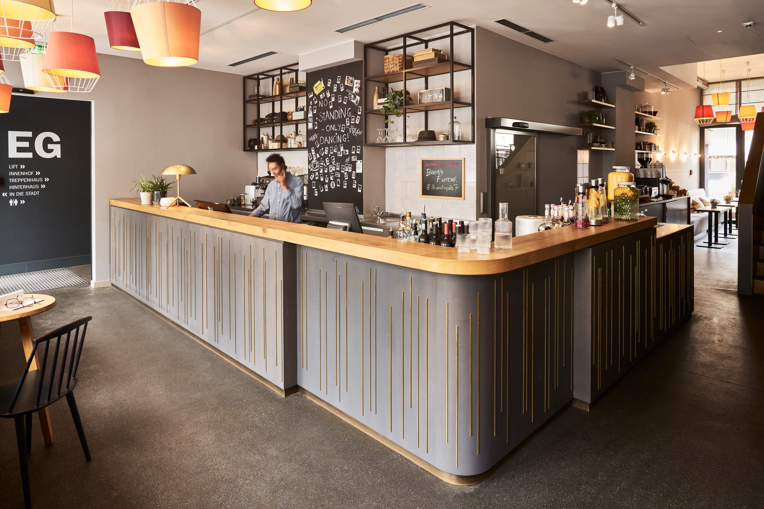Modern designte Empfangstheke mit angeschlossener Bar, Mitarbeiter in blauem Hemd dahinter und telefoniert