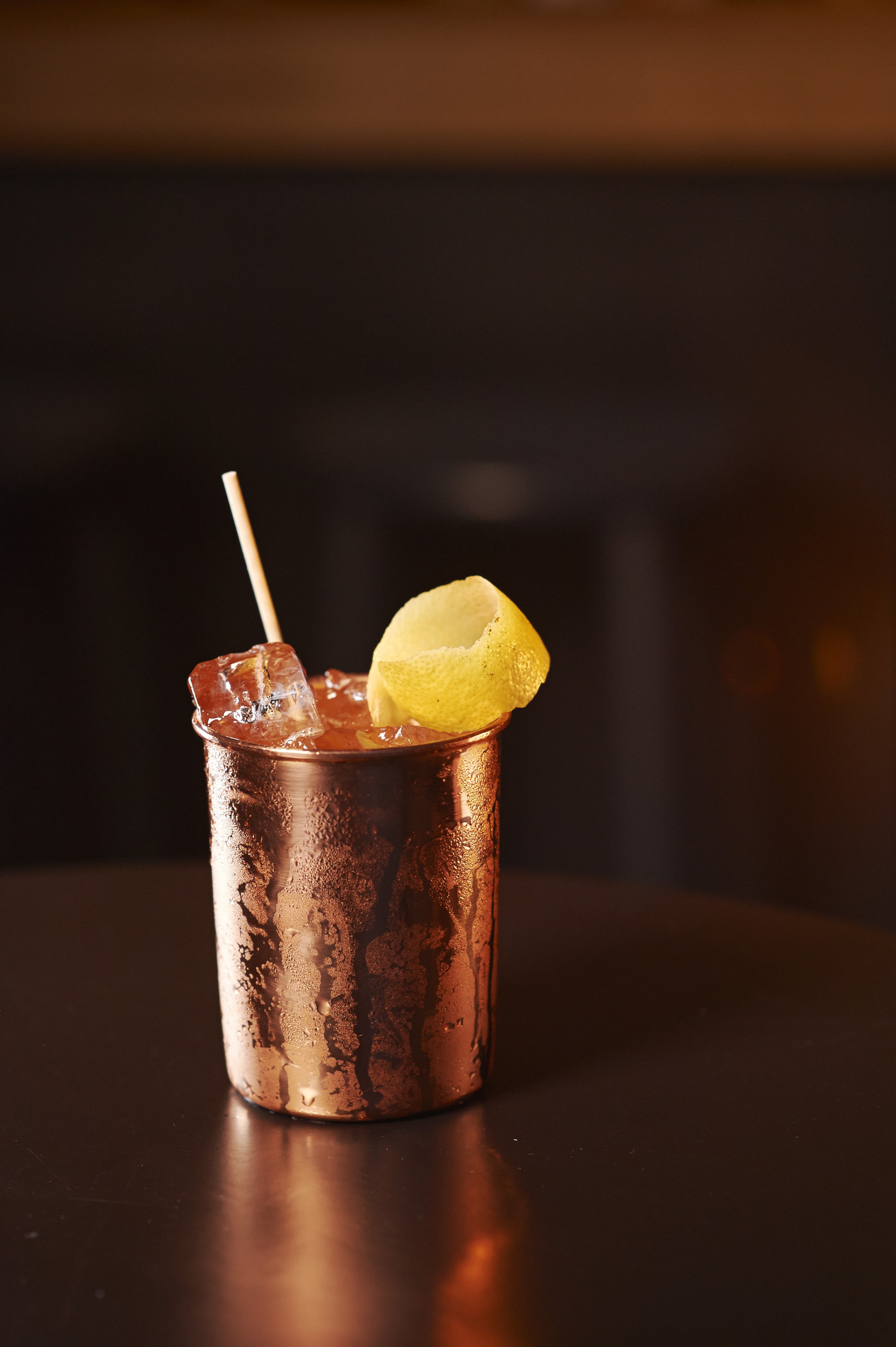 Ein leckerer Drink aus einem Kupferglas mit Zitronenschale und Eiswürfeln. 