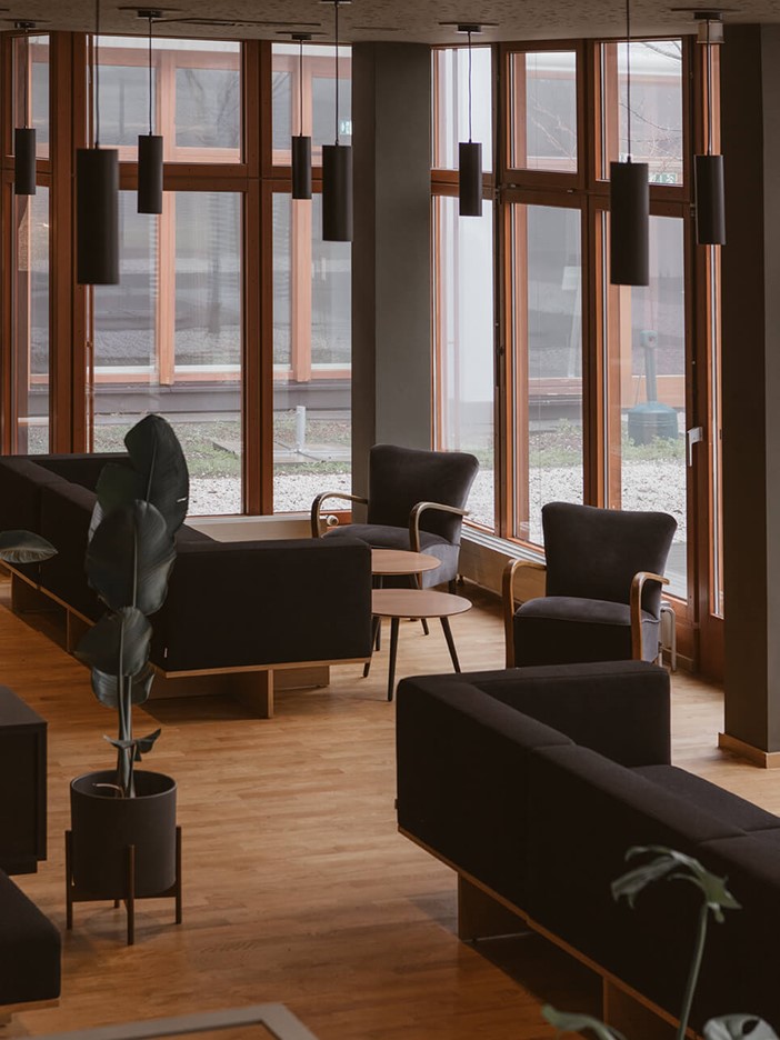 Lounge mit hochwertig designten schwarzen Sitzgelegenheiten, ausgewählten Accessoires und Pflanzen vor bodentiefen Fenstern. 