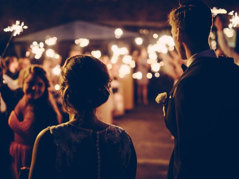 Ein Brautpaar wird im Dunkeln von seinen Gästen im Spalier stehend mit Wunderkerzen empfangen