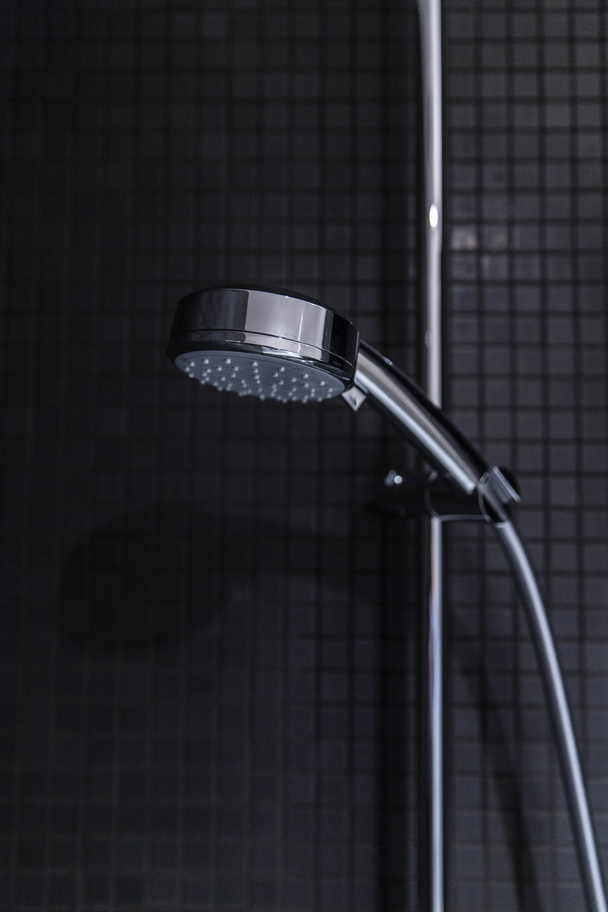 A chrome-plated shower head in its mount in front of an anthracite tiled wall. 