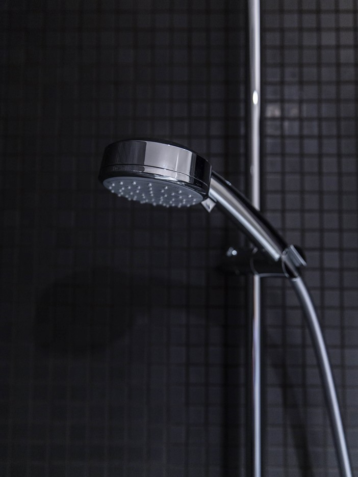 A chrome-plated shower head in its mount in front of an anthracite tiled wall. 
