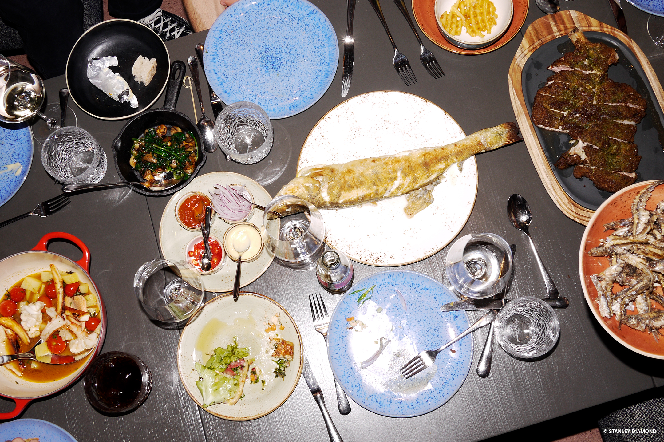 Dunkler Tisch auf dem leer gegessene Teller und Schalen und Platten mit verschiedenen Gerichten wie Fisch und Salat stehen