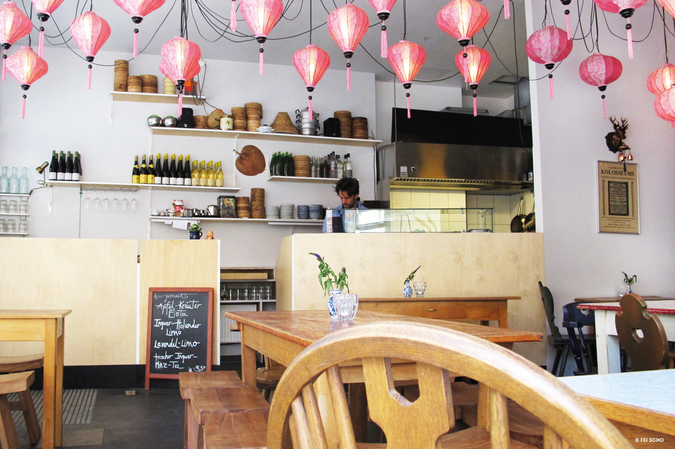 Restaurant with traditional-looking wooden chairs, benches and tables and a light wooden counter, pink Asian lanterns hanging from the ceiling