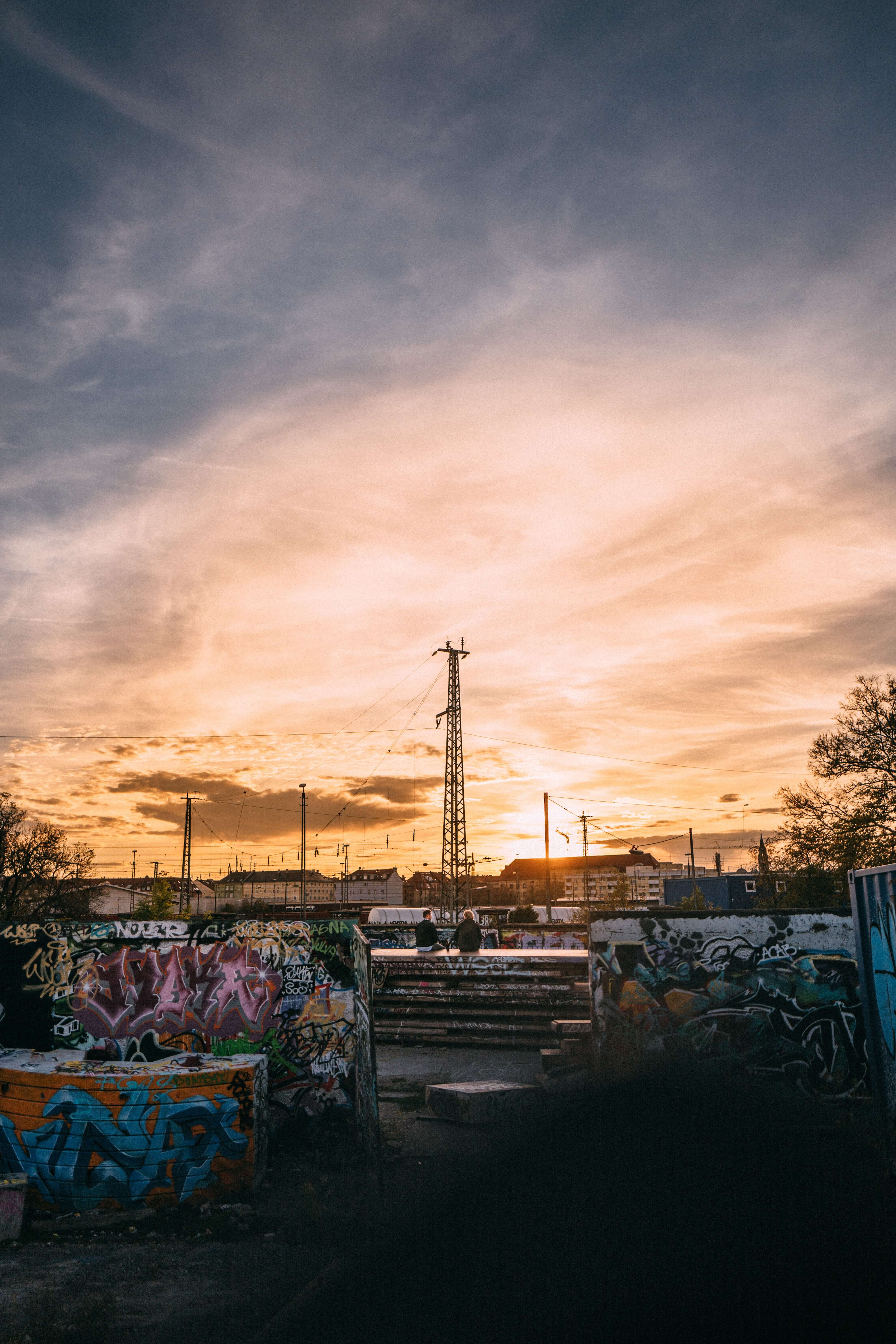 In einem heruntergekommenen Hof mit halbhohen Mauern voller bunter Graffiti sitzen zwei Jugendliche und betrachten den Sonnenuntergang in der Ferne