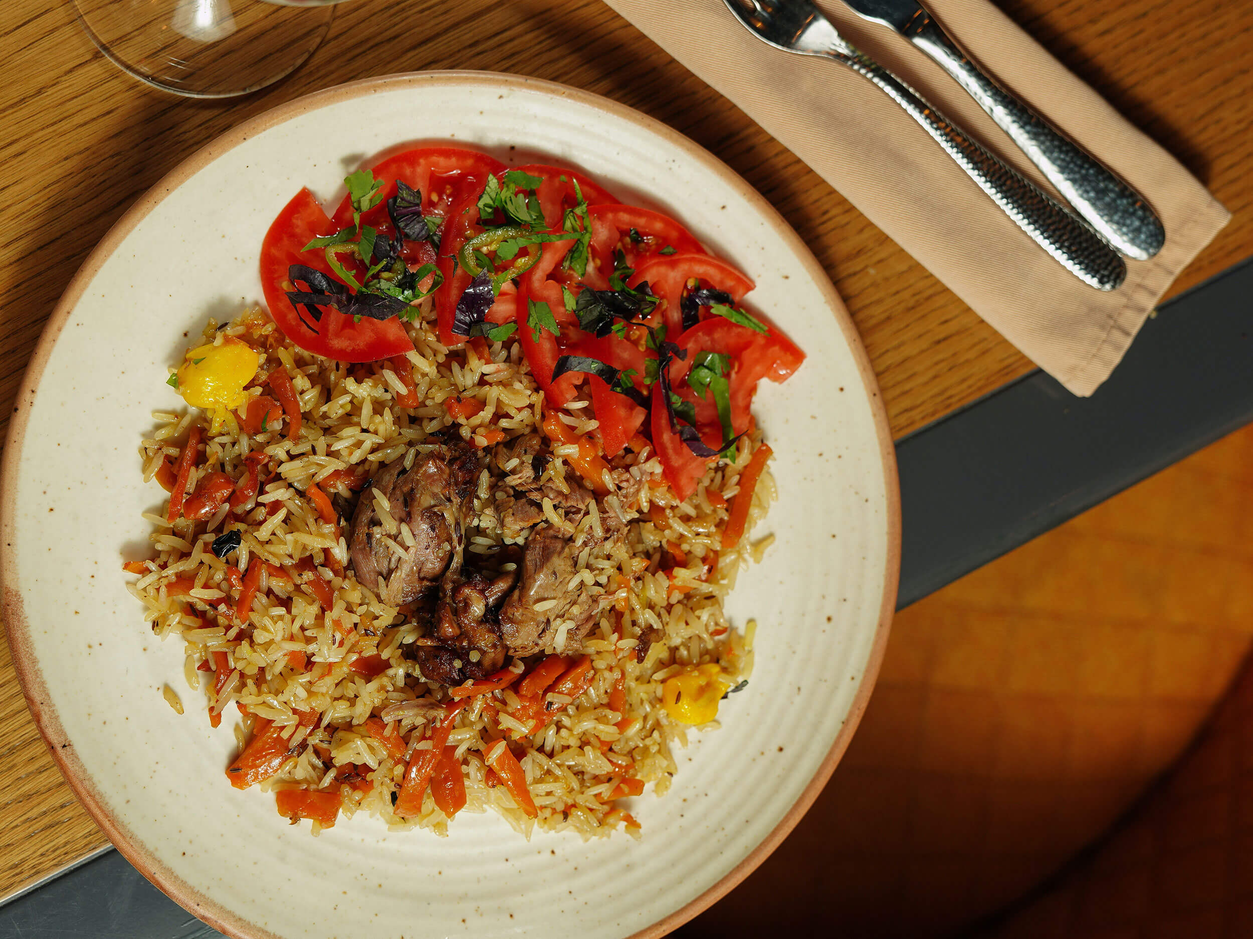 Teller mit orientalischem Reisgericht mit verschiedenen Kräutern, Fleisch und Gemüse auf einem Tisch