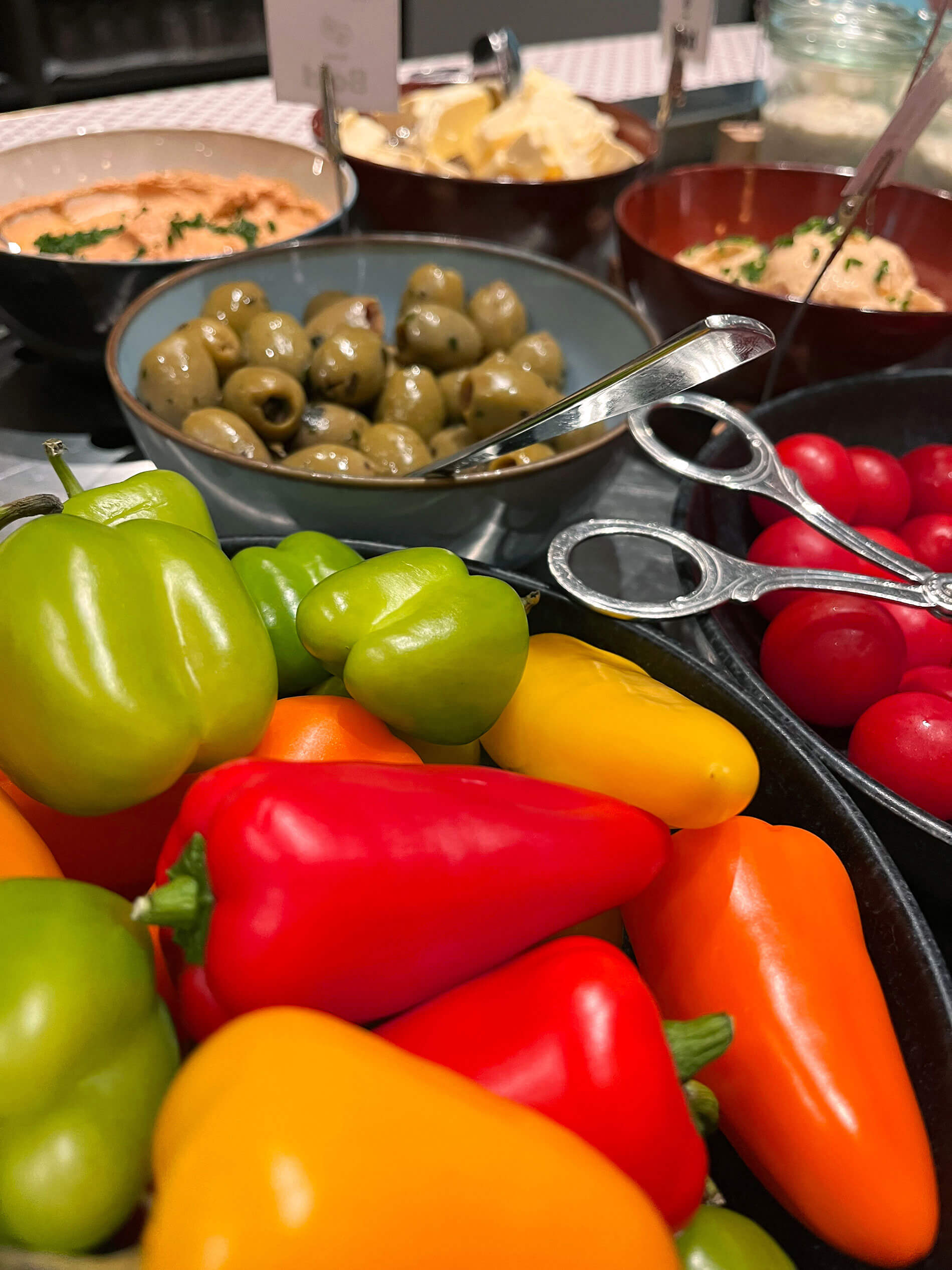 Paprika, Tomaten, Oliven und Aufstriche in Schalen am Buffet.