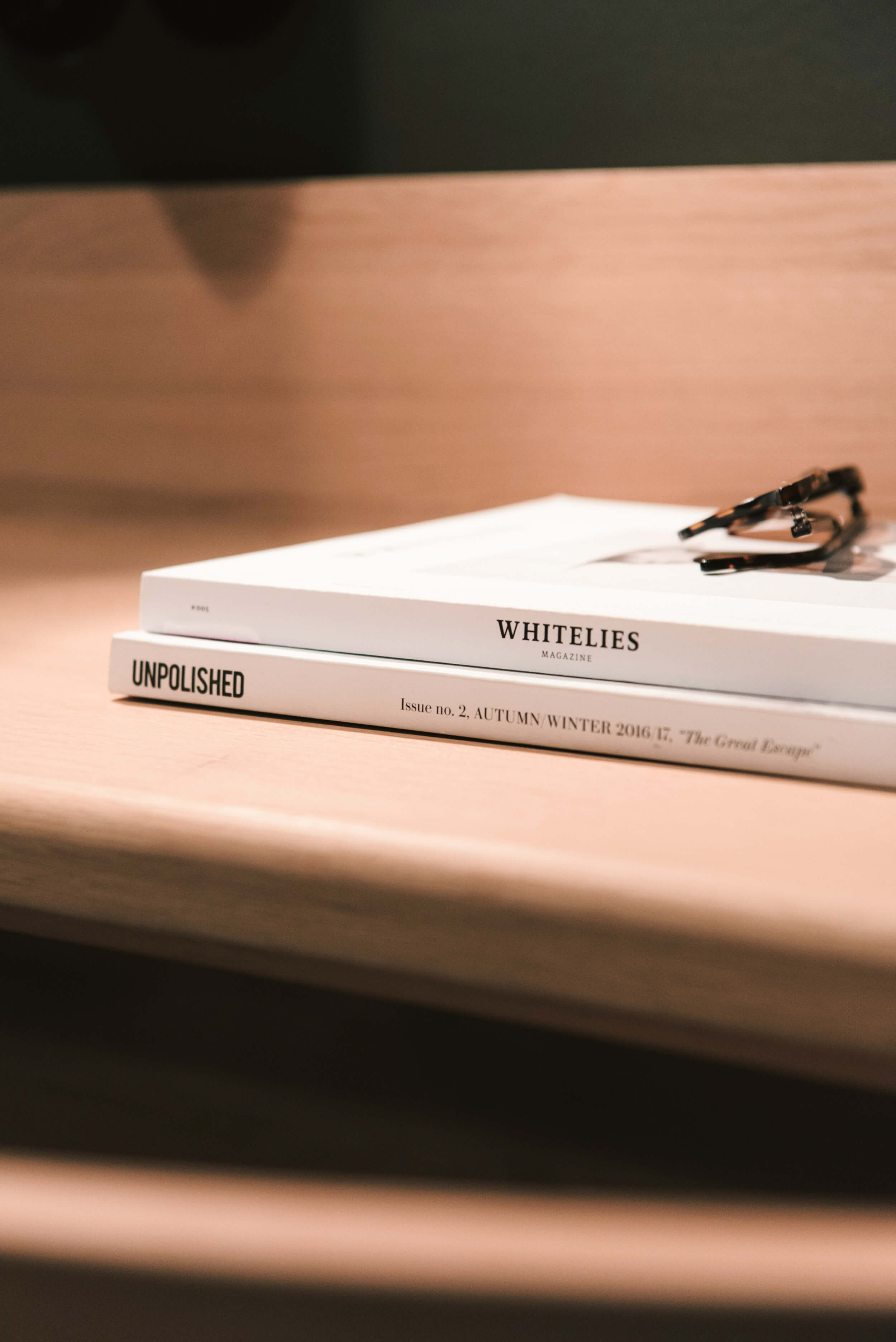 Stacked books on a  wooden shelf with horn-rimmed glasses on top