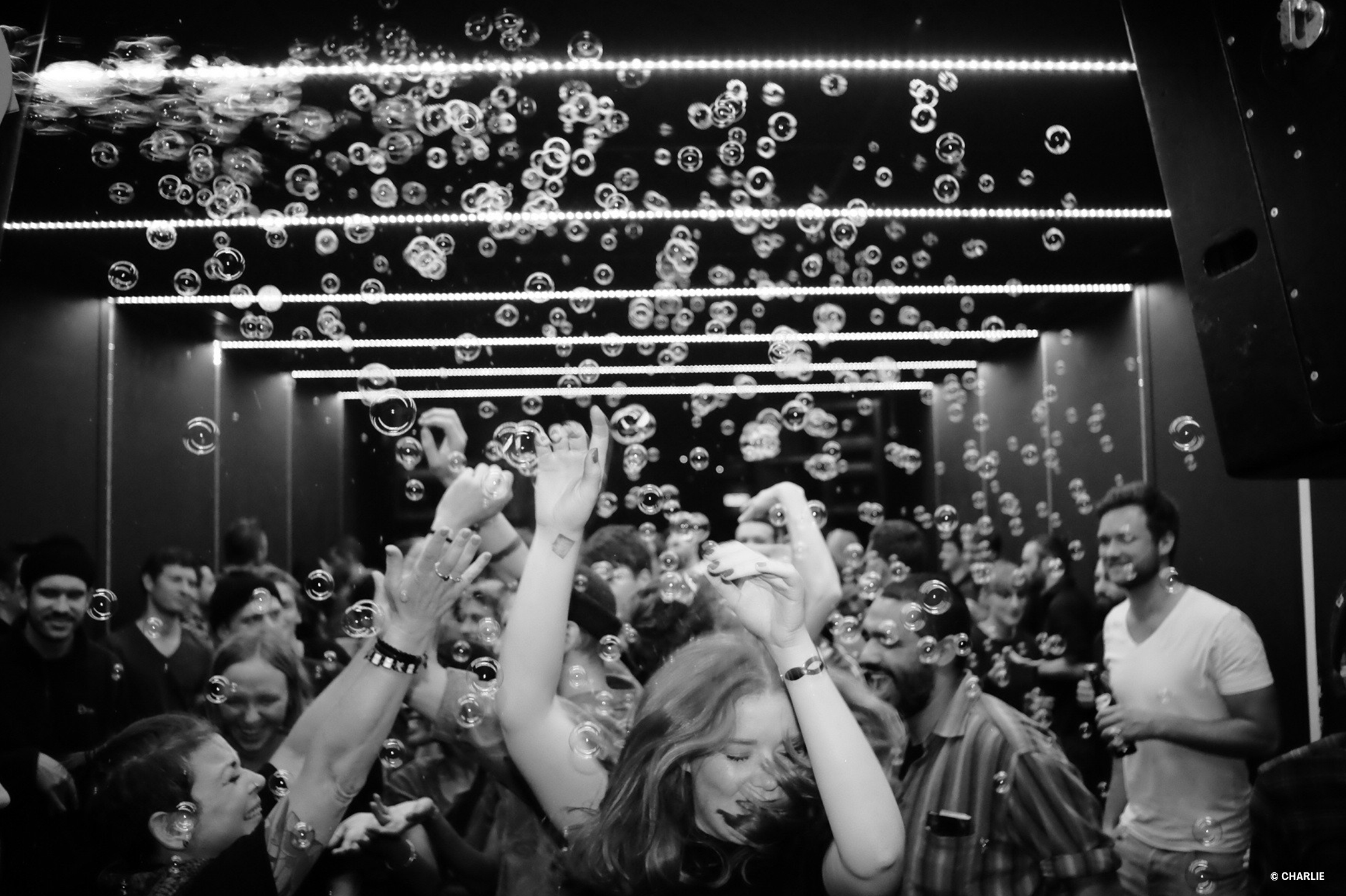 Many people celebrate and dance in a small club while soap bubbles rain down on them