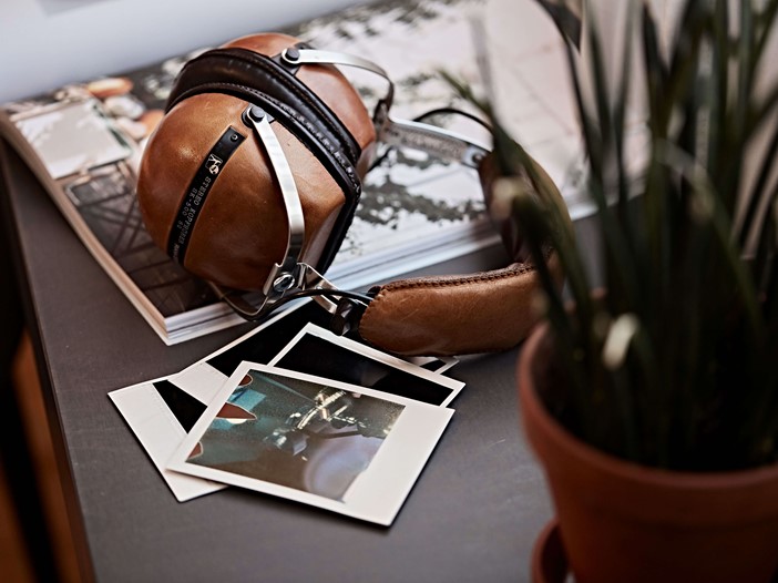 Close-up of retro headphones placed on top of a magazine. On the right Polaroid pictures, beside it a blurred plant.