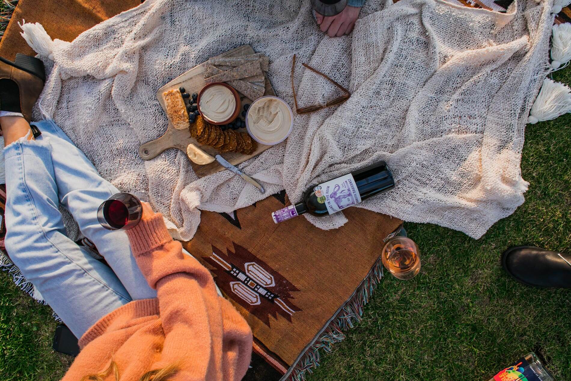 A person on a picnic blanket with wine and snacks