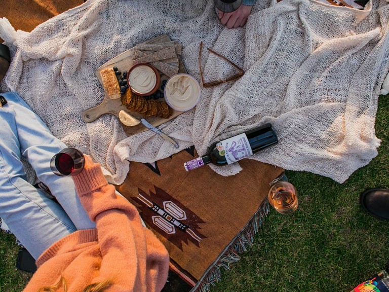 Eine Person auf einer Picknickdecke mit Wein und Knabbereien