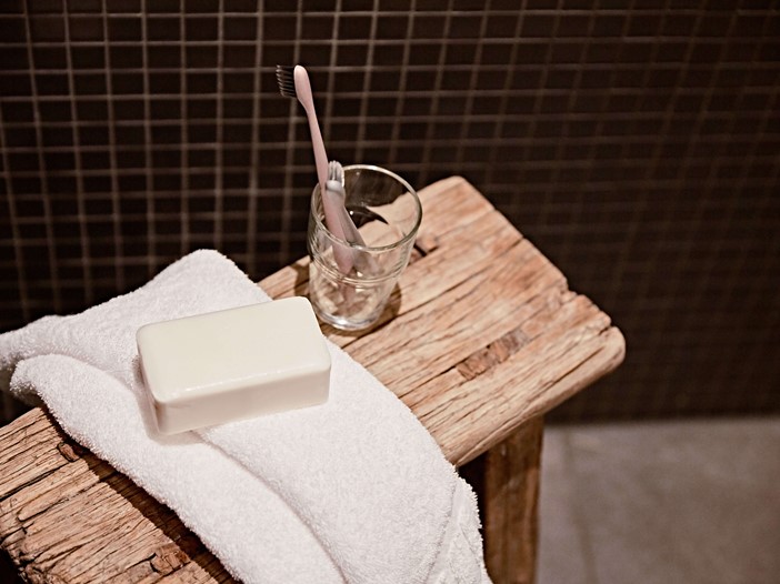 Detailaufnahme im Badezimmer, von einem Holzstuhl mit einem weißen Handtuch, Seife und Zahnbürsten im Glas. 