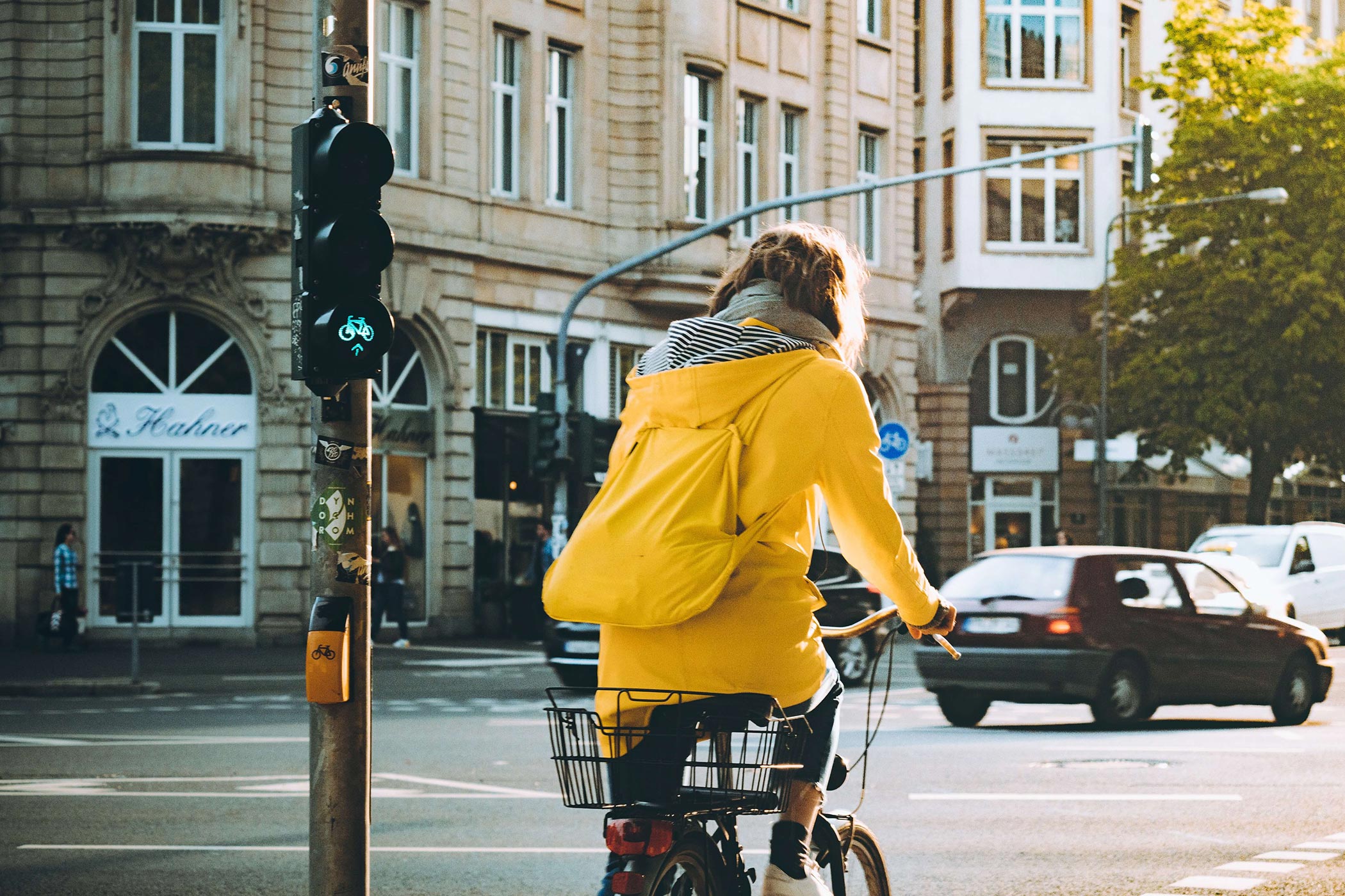 Woman with yellow backpack and yellow jacket on a bike at a bicycle traffic light in the middle of blocks of houses looking traditional