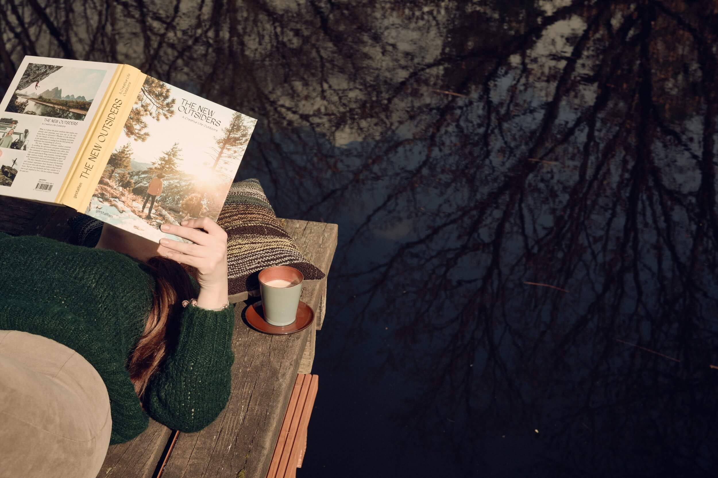 Female person reading a book in the sun by the pond at Bold Campus