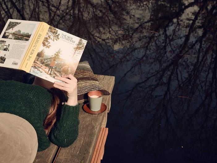Weibliche Person liest in der Sonne ein Buch am Rande des Teichs des Bold Campus
