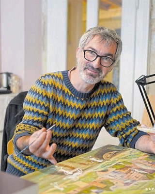 Sylvain Mérot, ein lächelnder Mann mit kurzen, grauen Haaren und Bart und Brille zeichnet auf eine Leinwand.