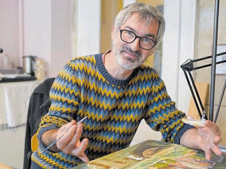Sylvain Mérot, ein lächelnder Mann mit kurzen, grauen Haaren und Bart und Brille zeichnet auf eine Leinwand.