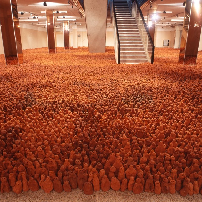 An art installation consisting of thousands of tiny lumps of clay, which are supposed to represent people, in a large room.