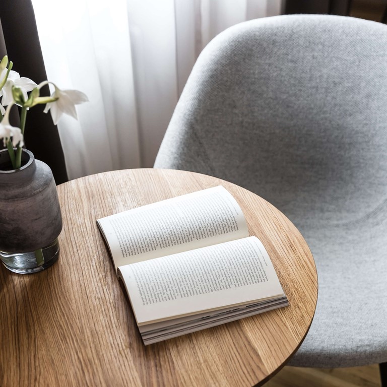Light grey armchair with a small wooden table and an opened book on the table