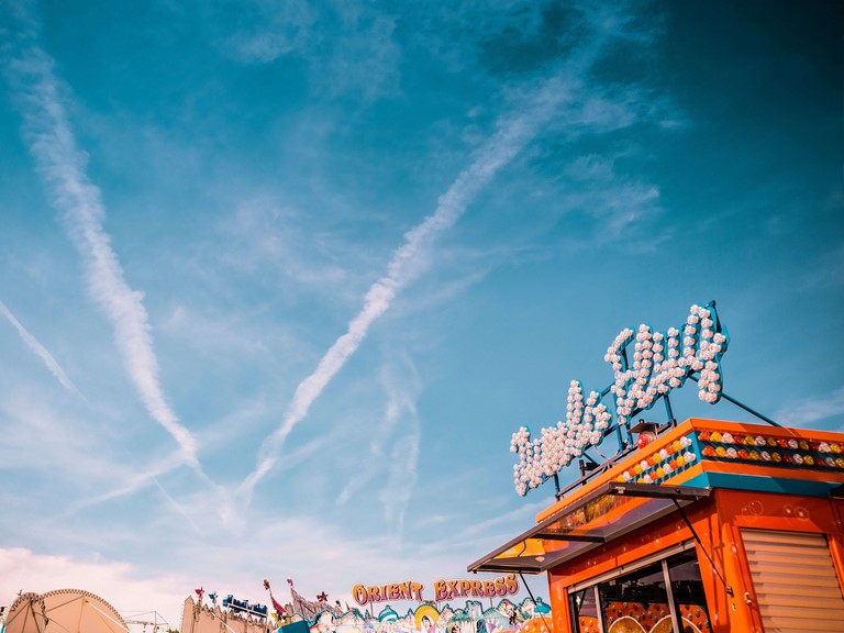 Blue sky with light clouds, below the colourful roofs of the attractions of a fairground