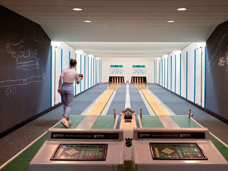 Two skittle alleys from the 70s with displays, the walls are painted with chalk, on the left a young woman in jeans sets to throw. 