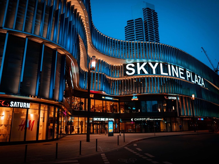 Futuristic looking shopping mall with names of the shops and a big lettering saying "Skyline Plaza"