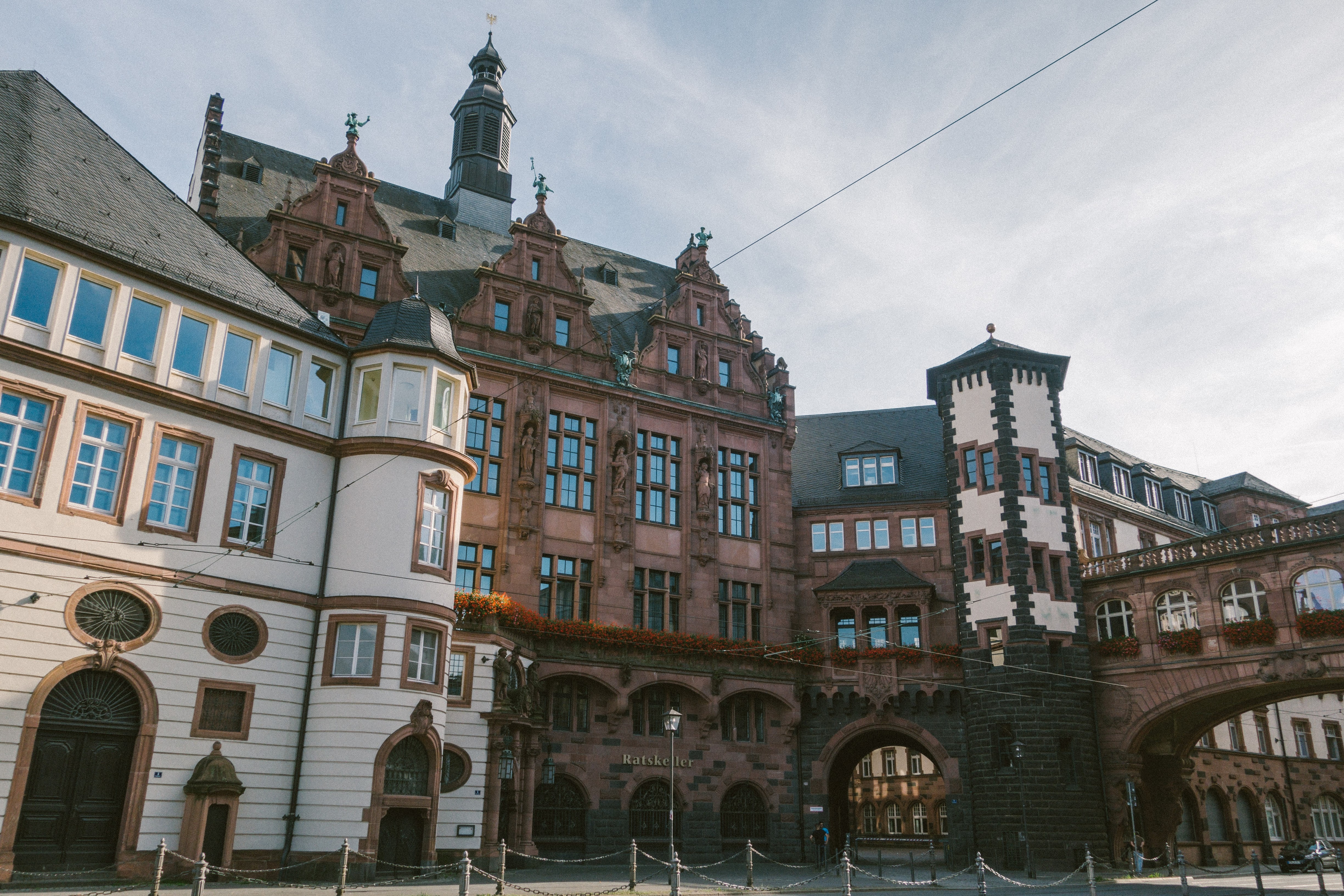 A historic house front made of sandstone and with gable roofs, to the right of which a covered bridge with windows leads off
