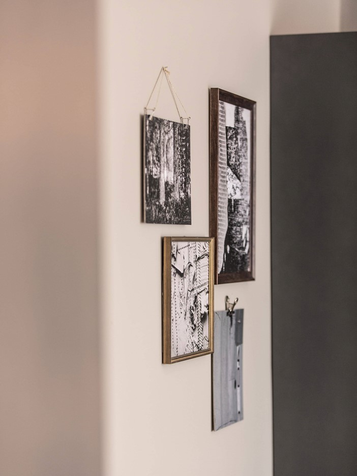 Schwarz-weiße Bilder, die mit und ohne Rahmen neben einem dunkelgrauen Schrank an der Wand hängen. 